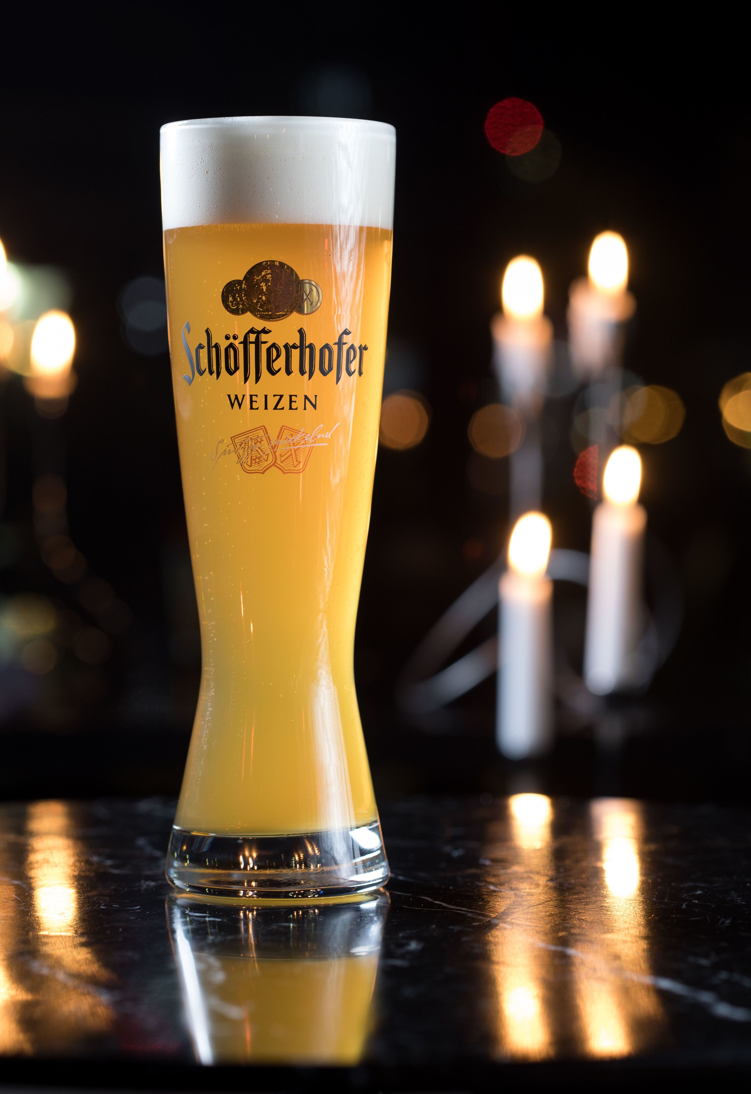 Un grand verre de bière, surmonté d’une mousse abondante, portant l’étiquette « Schofferhofer Weizen », posé sur une surface réfléchissante.