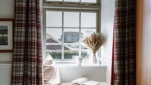 Ein Zimmer mit Fenster, einer weißen Bank, einem Korb und karierten Vorhängen.