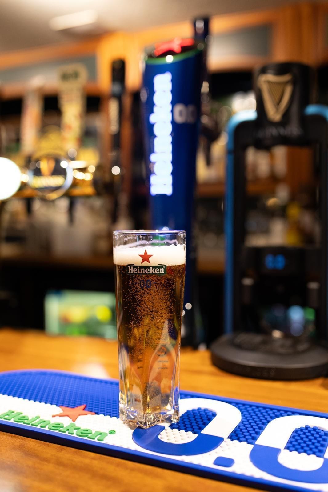 A tall glass of beer with a Heineken logo on a bar counter.