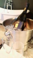 Una botella de vino en un balde de metal con hielo, rodeada de copas para shots.