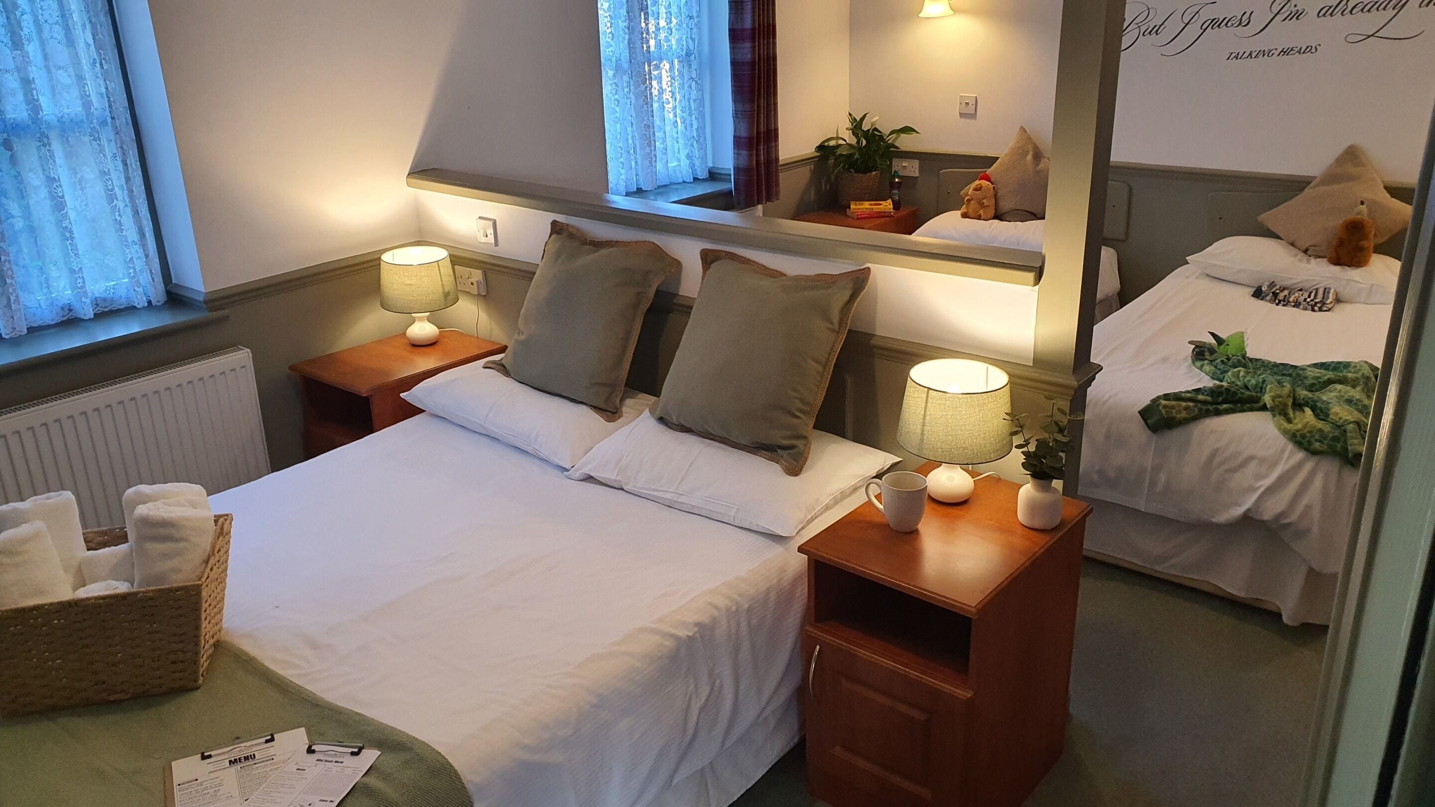 A hotel room with a bed, bedside tables, a lamp, a mirror, a window with curtains, and a wall with a sign.