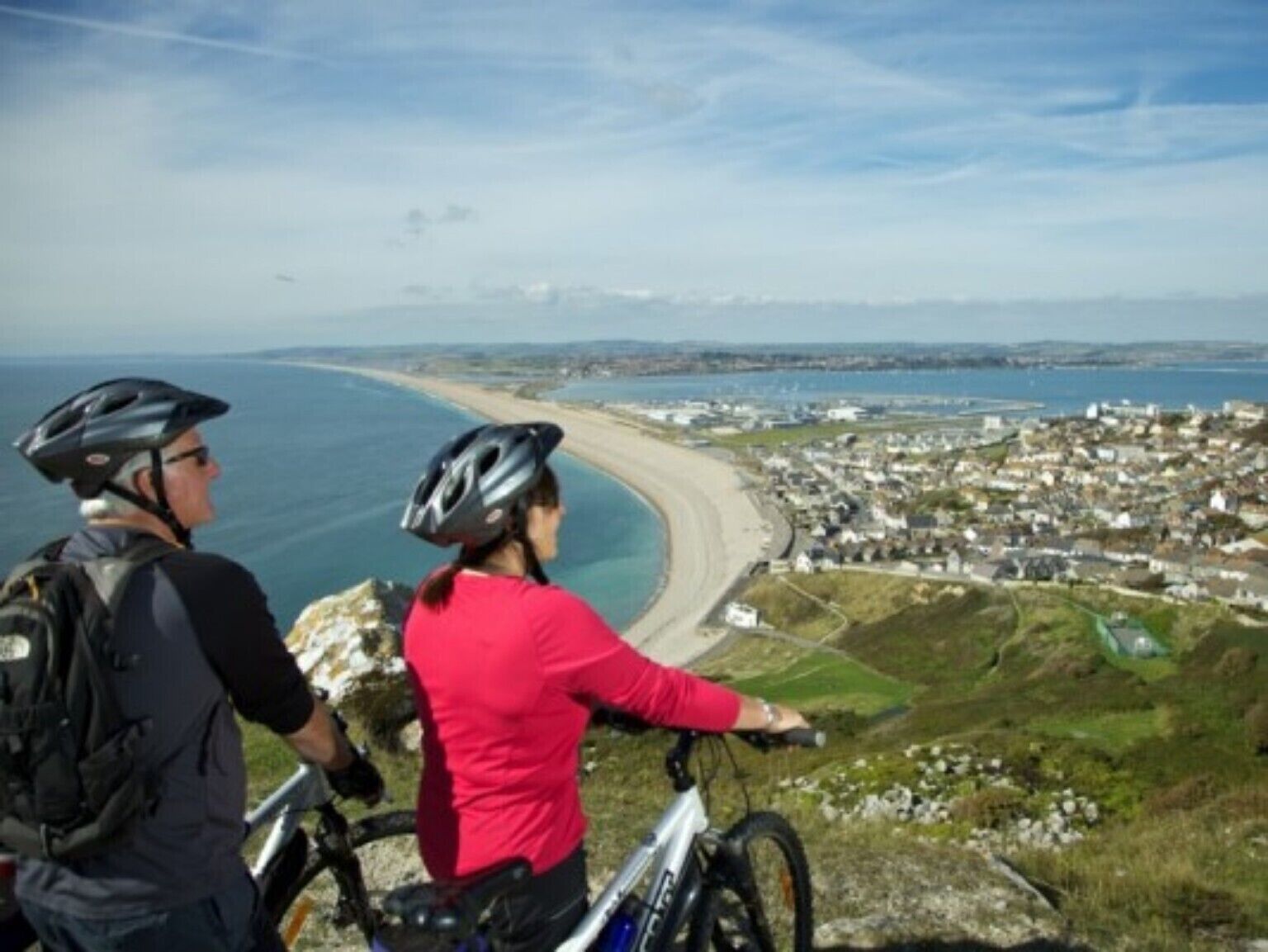 Two people on a mountain bike overlooking a coastal town.