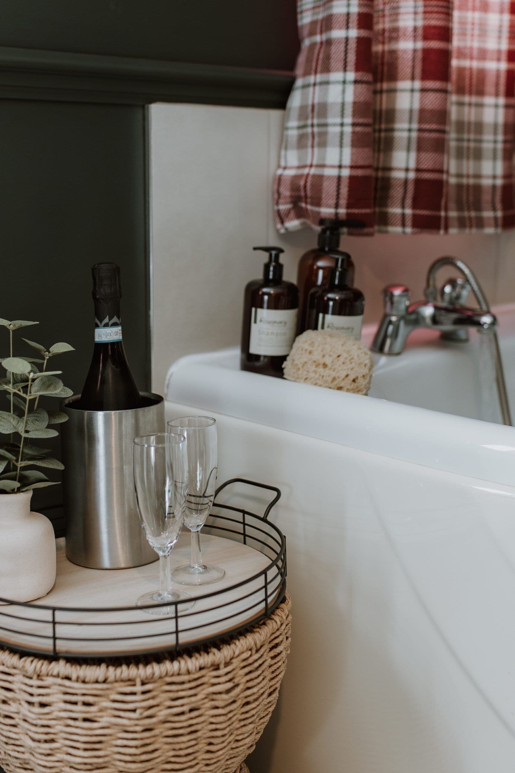 A bathroom with a bathtub, a bottle of champagne, two glasses, a candle, and toiletries.
