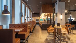 A modern restaurant with wooden tables and booths, large windows, and pendant lighting.