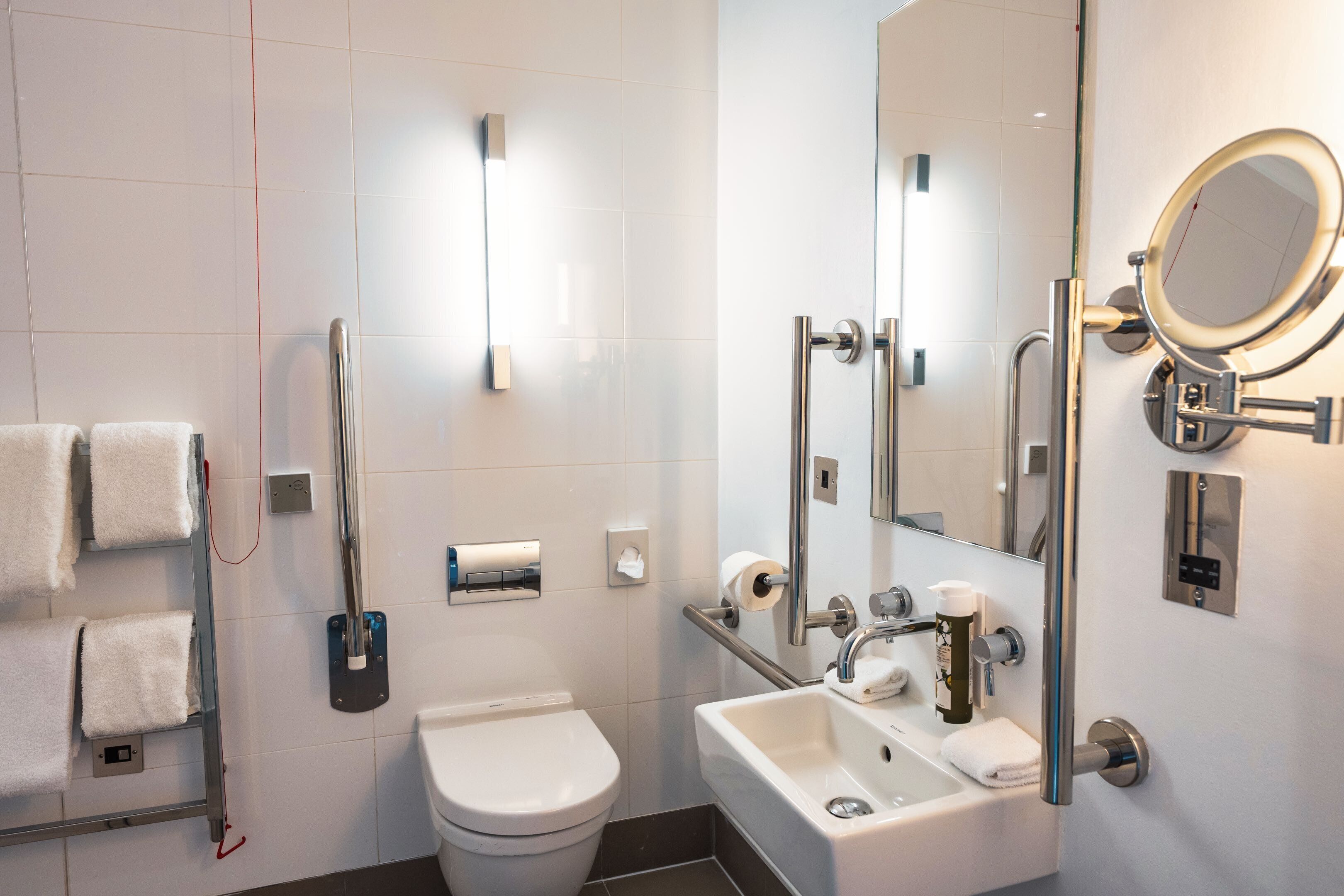 Un baño moderno con inodoro, lavamanos y barras de apoyo.