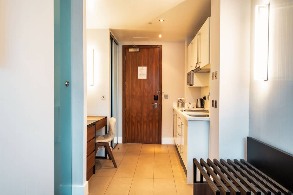 A narrow hallway with a wooden door, a small table with a chair, and a bench.