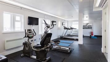 Un gimnasio con bicicletas estáticas, cintas de correr y colchonetas de ejercicio.
