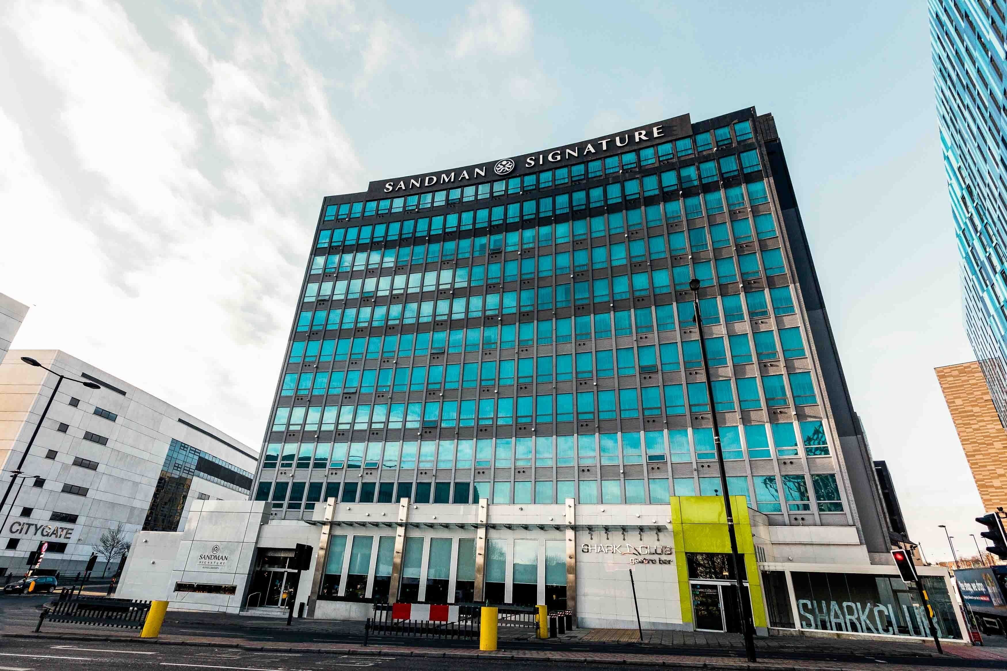 Un bâtiment moderne avec une façade en verre et l’inscription « Sandman Signature » au sommet.