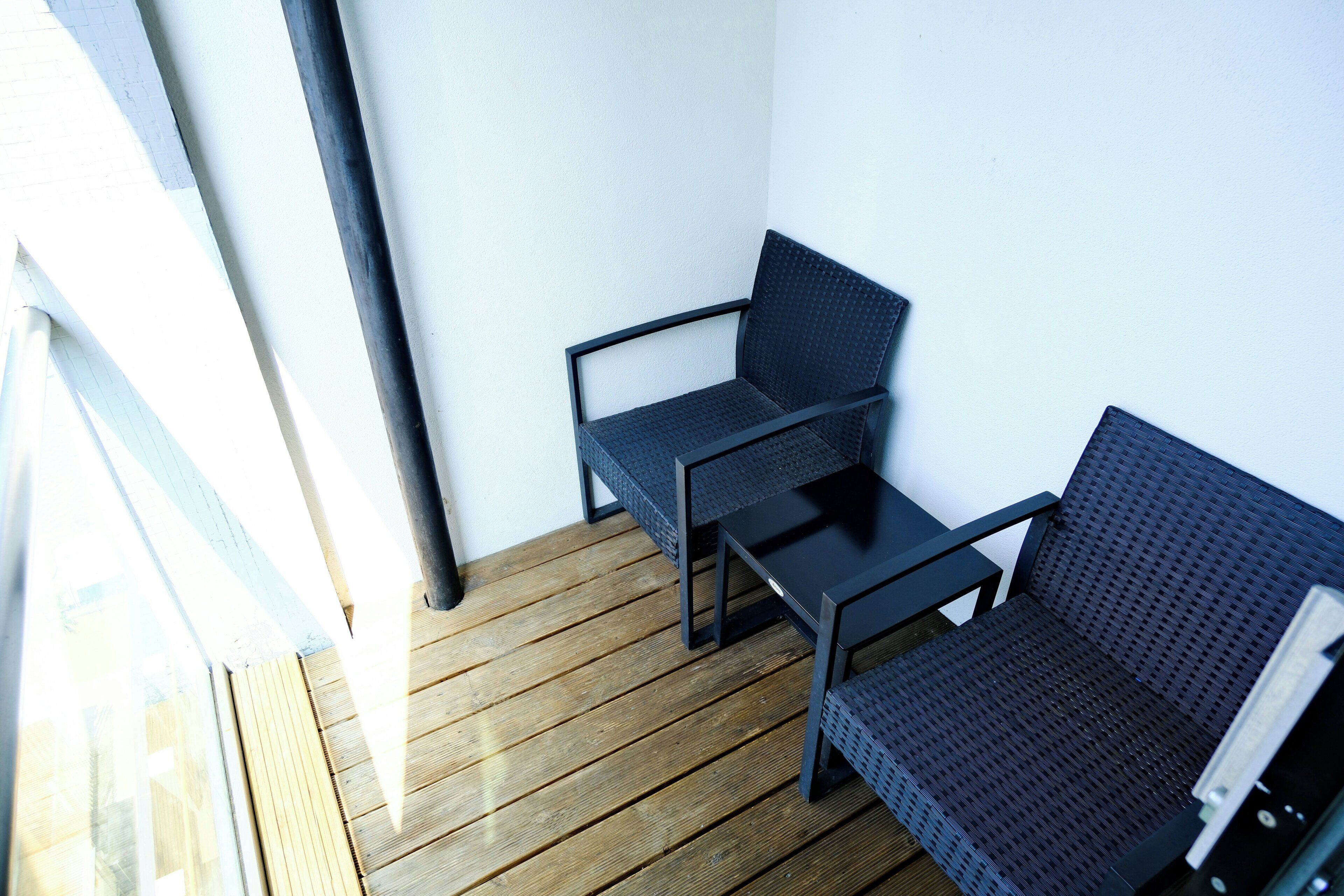 Ein Blick in einen Raum mit Holzboden, einem schwarzen Metallstuhl und einer schwarzen Metalsofa.
