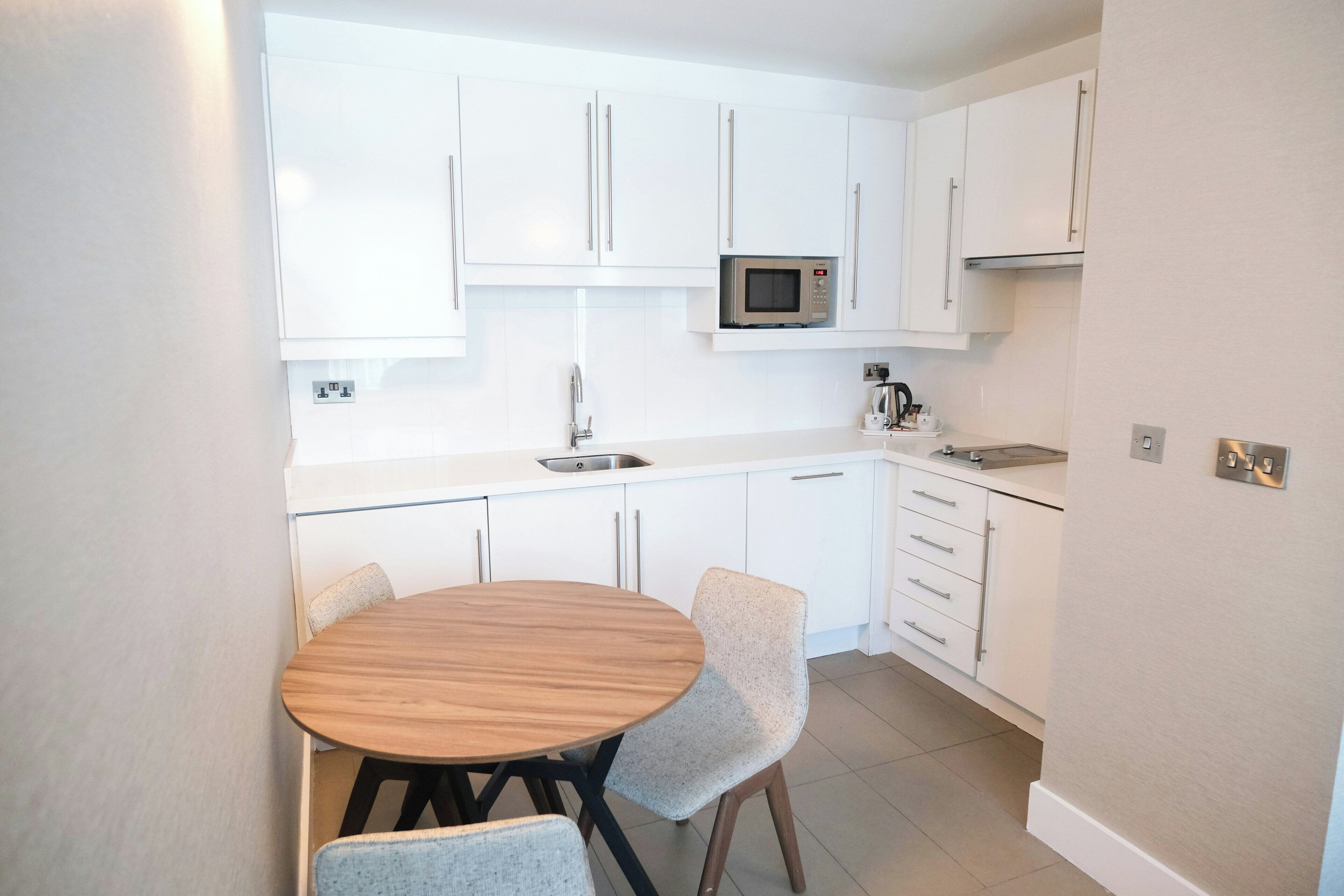 A compact kitchen with white cabinets, a microwave, a sink, and a dining table with chairs.