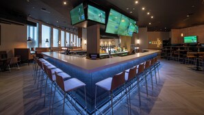 A modern bar area with a long counter, multiple screens, and bar stools.