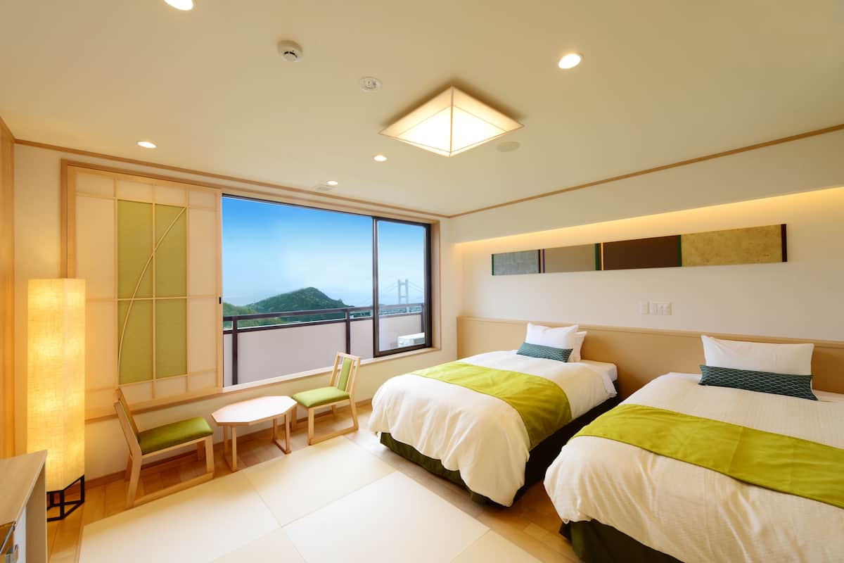 A hotel room with two beds, a desk, a chair, and a large window with a view of a bridge.