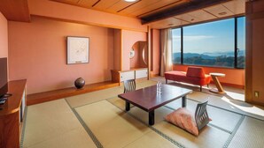 A modern hotel room with a wooden ceiling, tatami mat flooring, a sofa, a table, and a large window offering a scenic view. - WASHU BULE RESORT Kasago (Kurashiki)