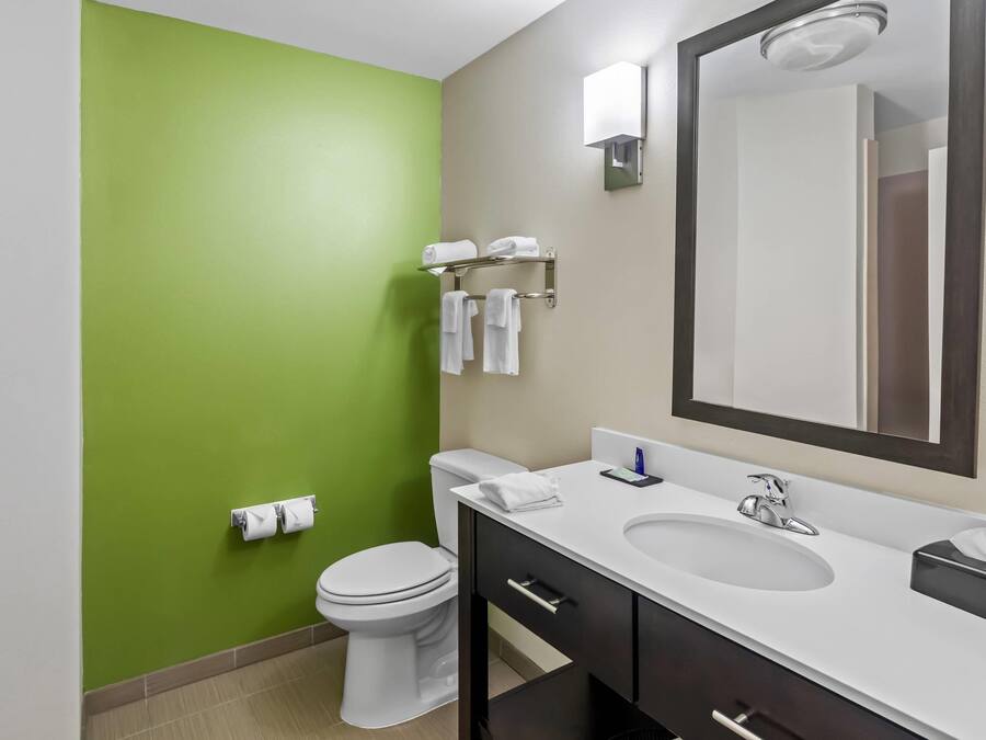 A bathroom with a green wall, white toilet, and a vanity with a mirror, sink, and towel rack.