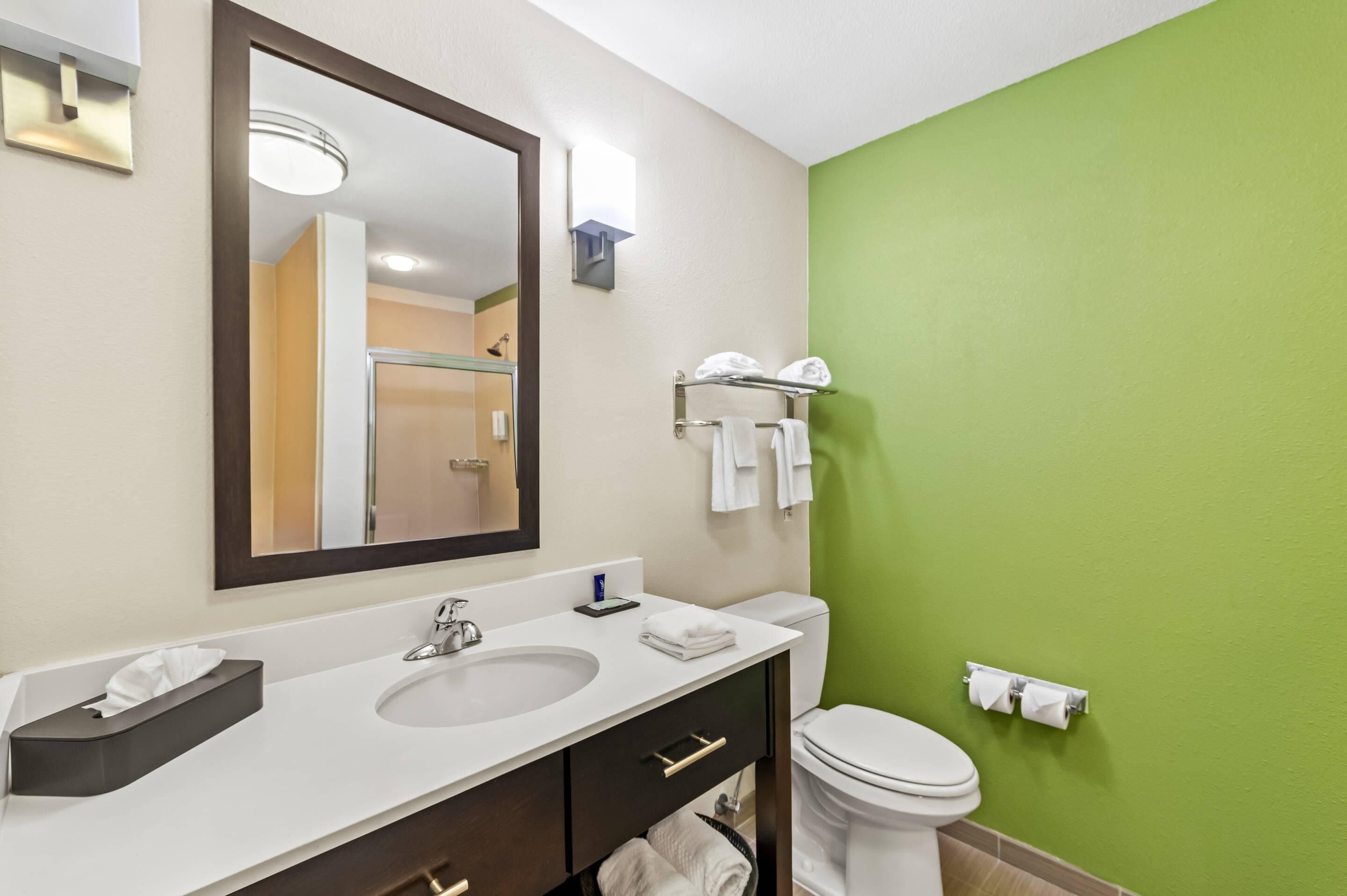 Une salle de bain avec un lavabo blanc, un miroir, des toilettes et un mur vert.
