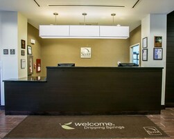 Una mesa de recepción con un letrero de Sleep Inn & Suites, una computadora Dell y una alfombra de bienvenida para Dripping Springs.