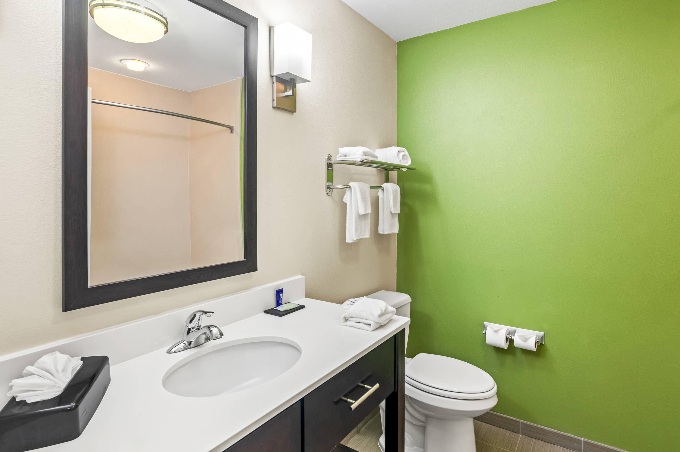A bathroom with a white sink, mirror, and toilet. There are towels on a rack and a tissue box on the counter.