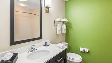 Une salle de bain avec un lavabo blanc, un miroir et des toilettes. On y trouve des serviettes sur un porte-serviettes et une boîte de mouchoirs sur le comptoir.