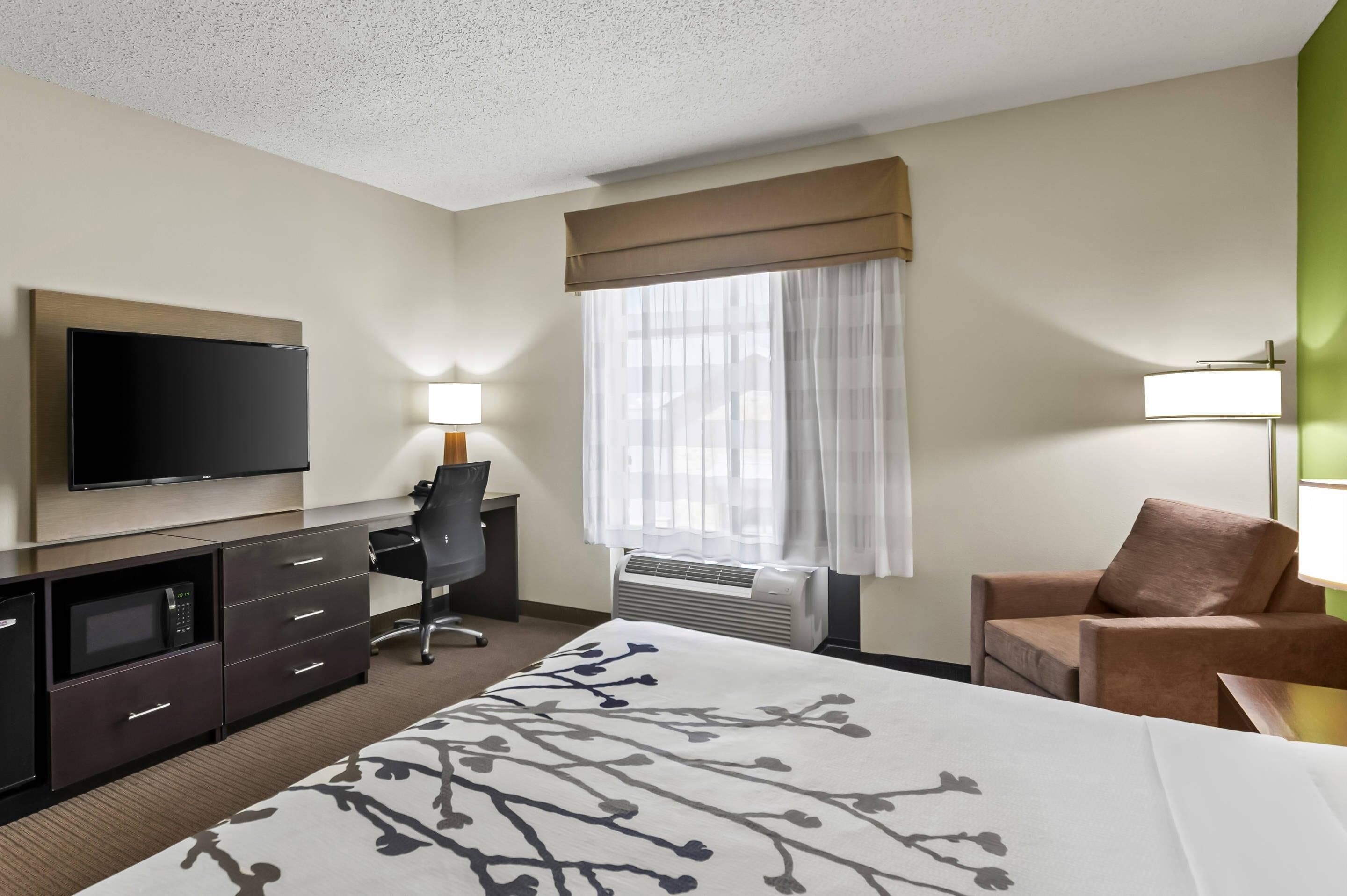 A hotel room with a bed, a desk, a chair, a television, and a window with curtains.