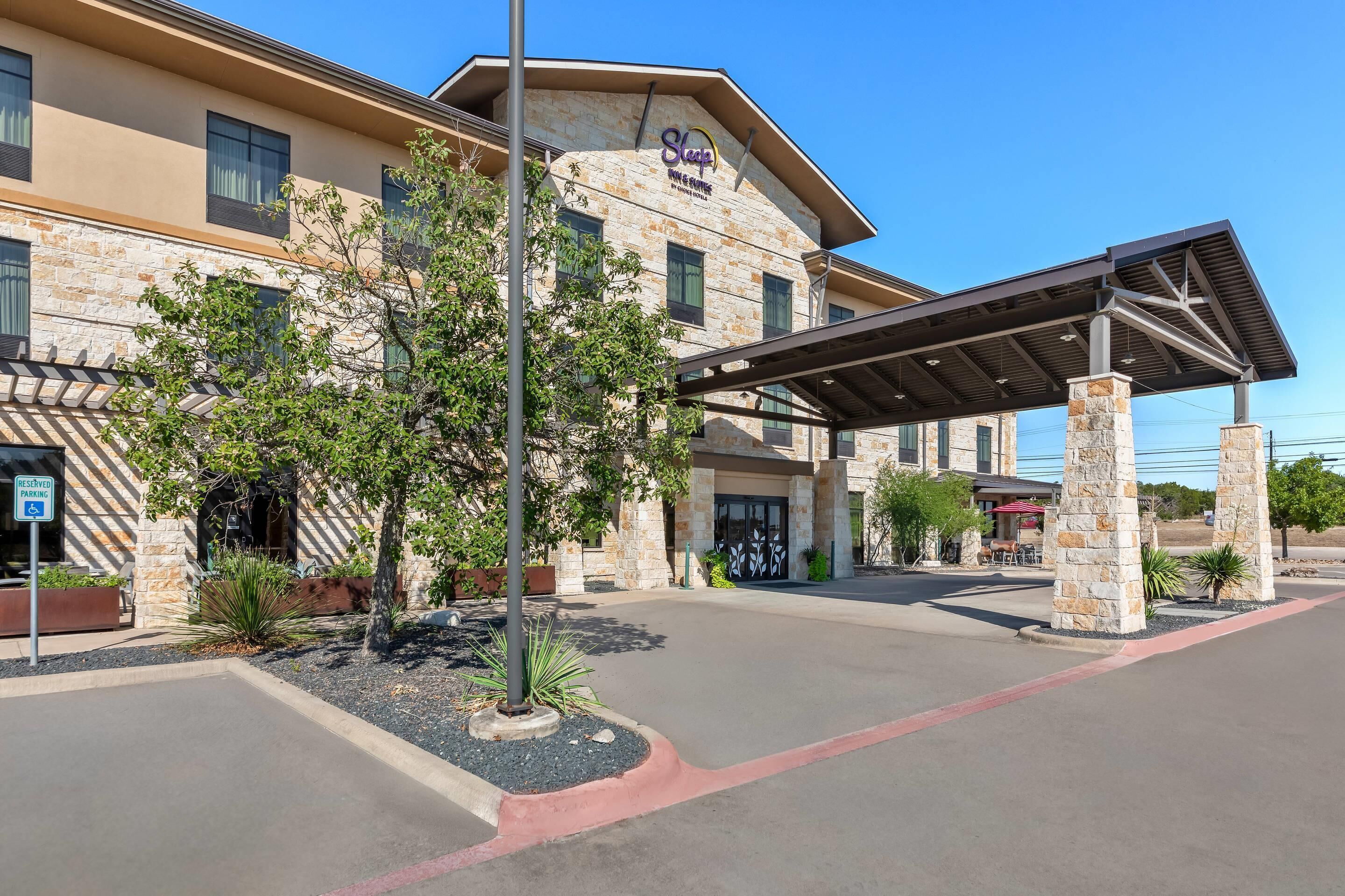 A hotel with a stone facade, a covered entrance, and a landscaped area with trees and shrubs.