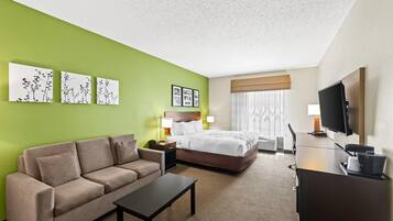 Habitación de hotel con una pared verde, una cama, un sofá, un escritorio, un televisor y obras de arte.