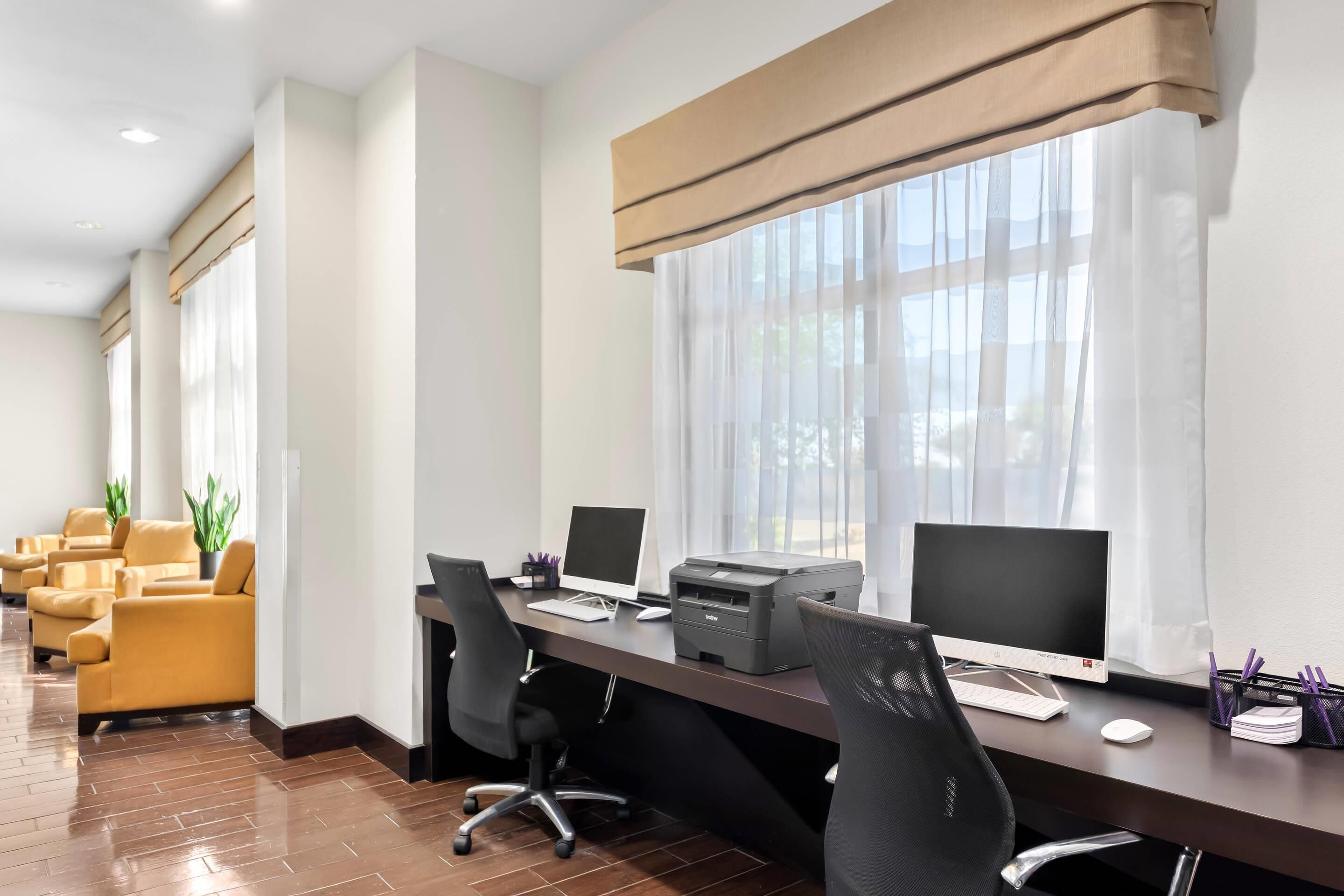 A modern office space with a long desk, multiple chairs, and two computer monitors.