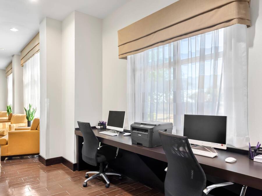 A modern office space with a long desk, multiple chairs, and two computer monitors.