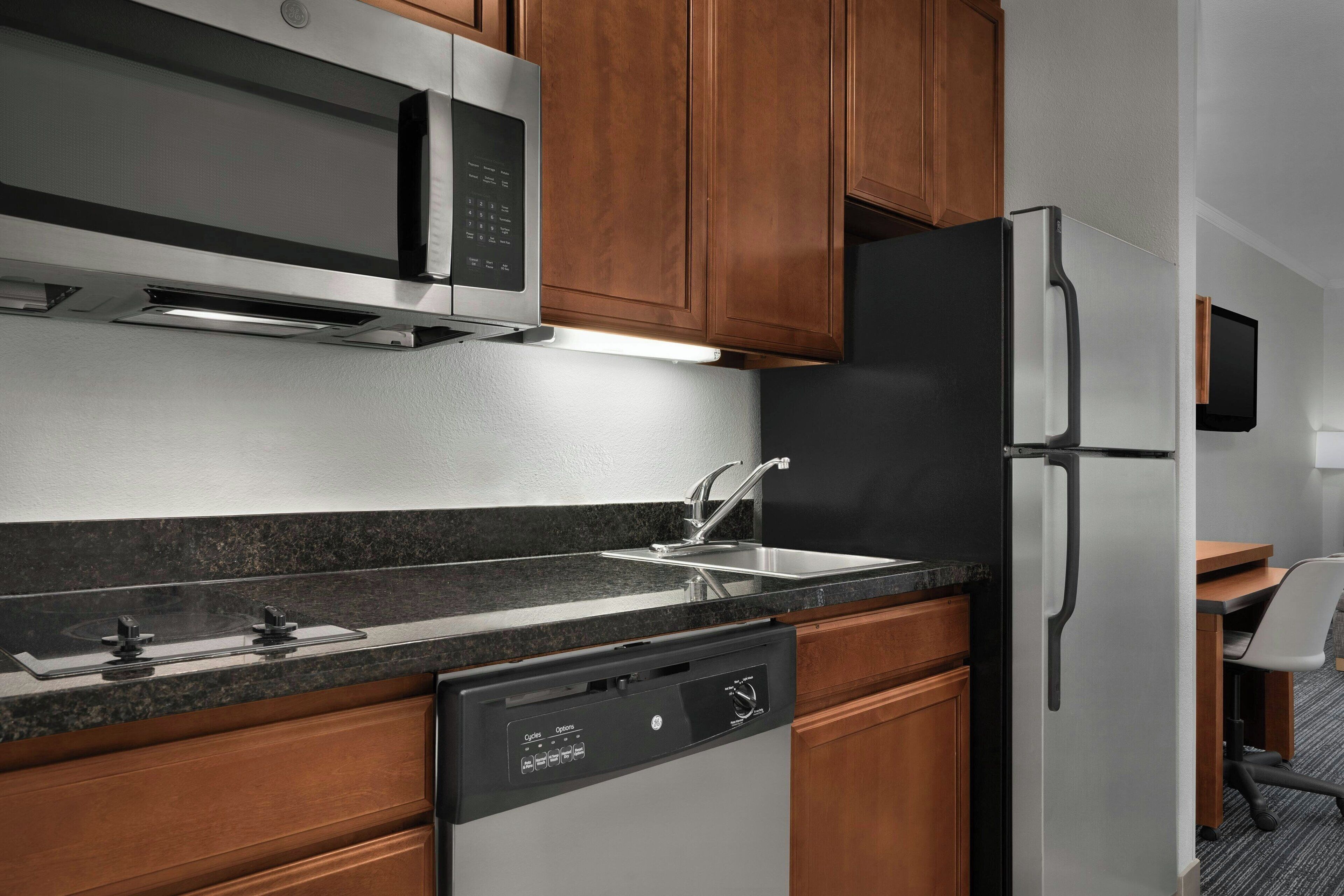 A kitchen with wooden cabinets, a stainless steel refrigerator, a microwave, and a dishwasher.