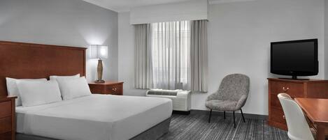 A hotel room with a large bed, a desk, a chair, a television, a lamp, and a window with curtains.