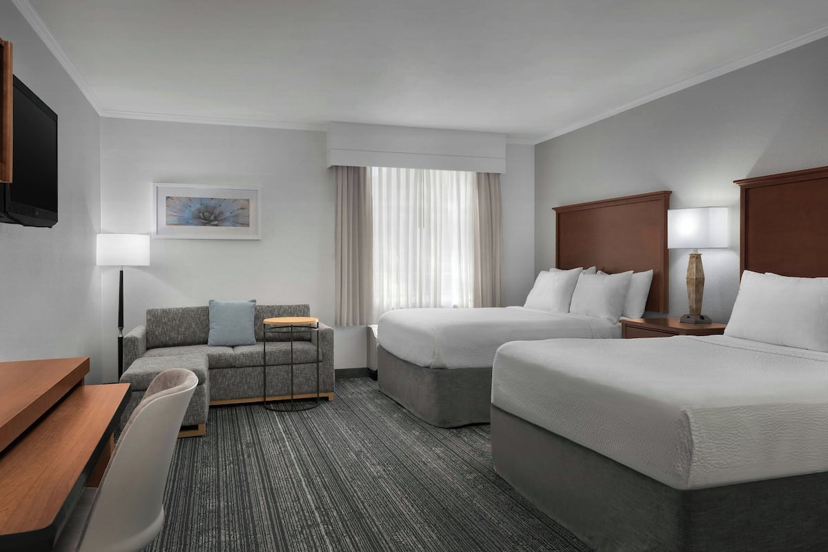 A hotel room with two beds, a desk, a chair, a TV, and a window with curtains.