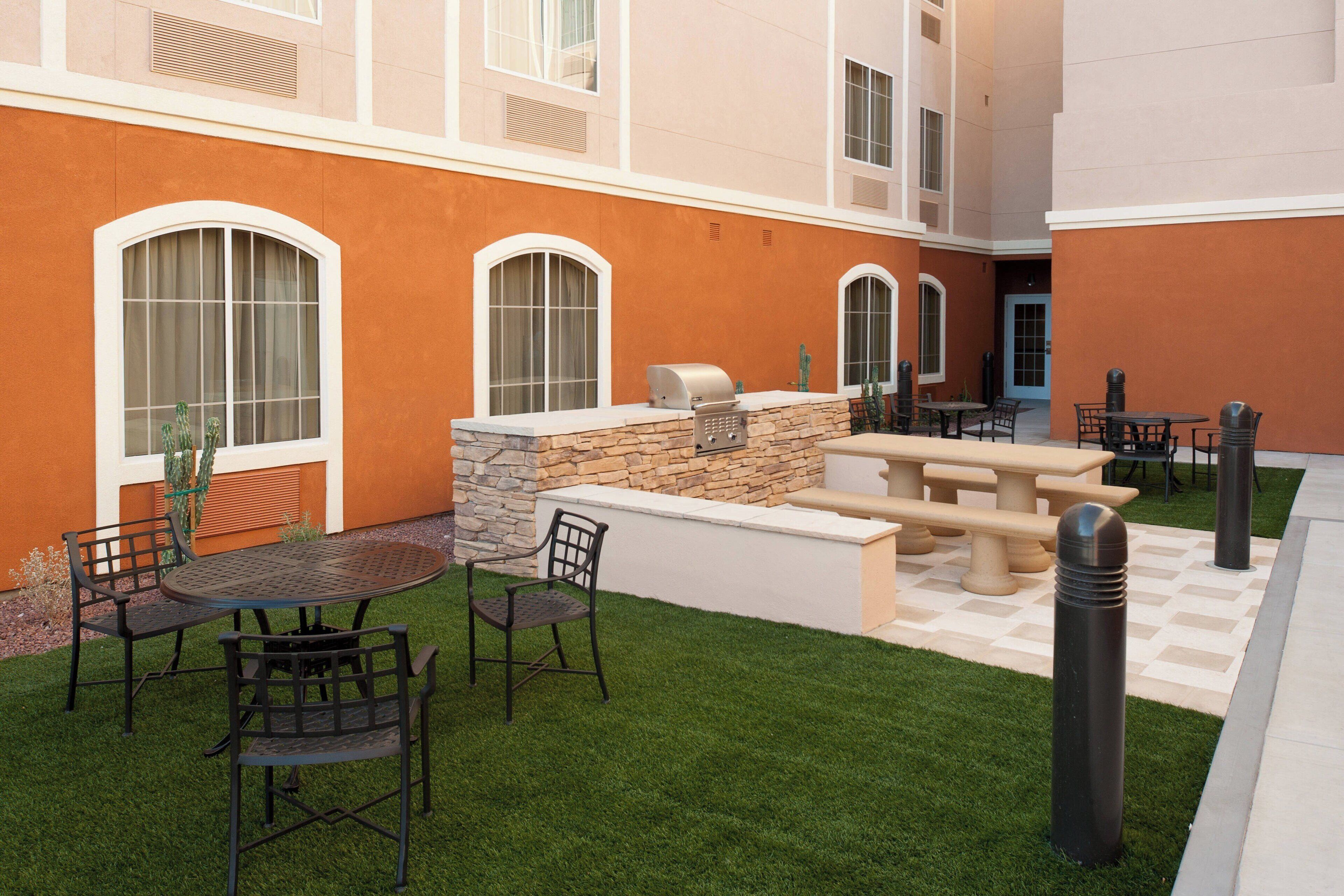 An outdoor patio area with a stone barbecue station, a round table with chairs, and a checkered floor pattern.