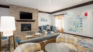 A hotel lobby with a stone fireplace, comfortable seating, a flat-screen TV, and a map on the wall. - TownePlace Suites Tucson Williams Centre (Tucson)