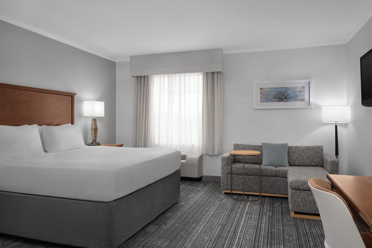 A hotel room with a large bed, a sofa, a desk, a TV, and a window with curtains.