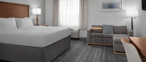 A hotel room with a large bed, a sofa, a desk, a TV, and a window with curtains.