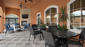 An outdoor patio with a stone floor, black wicker furniture, a flat-screen TV mounted on a stone wall, and large windows. - TownePlace Suites Tucson Williams Centre (Tucson)