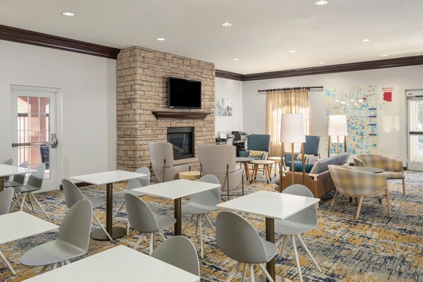 A hotel lobby with a stone fireplace, seating area, and tables. - TownePlace Suites Tucson Williams Centre (Tucson)