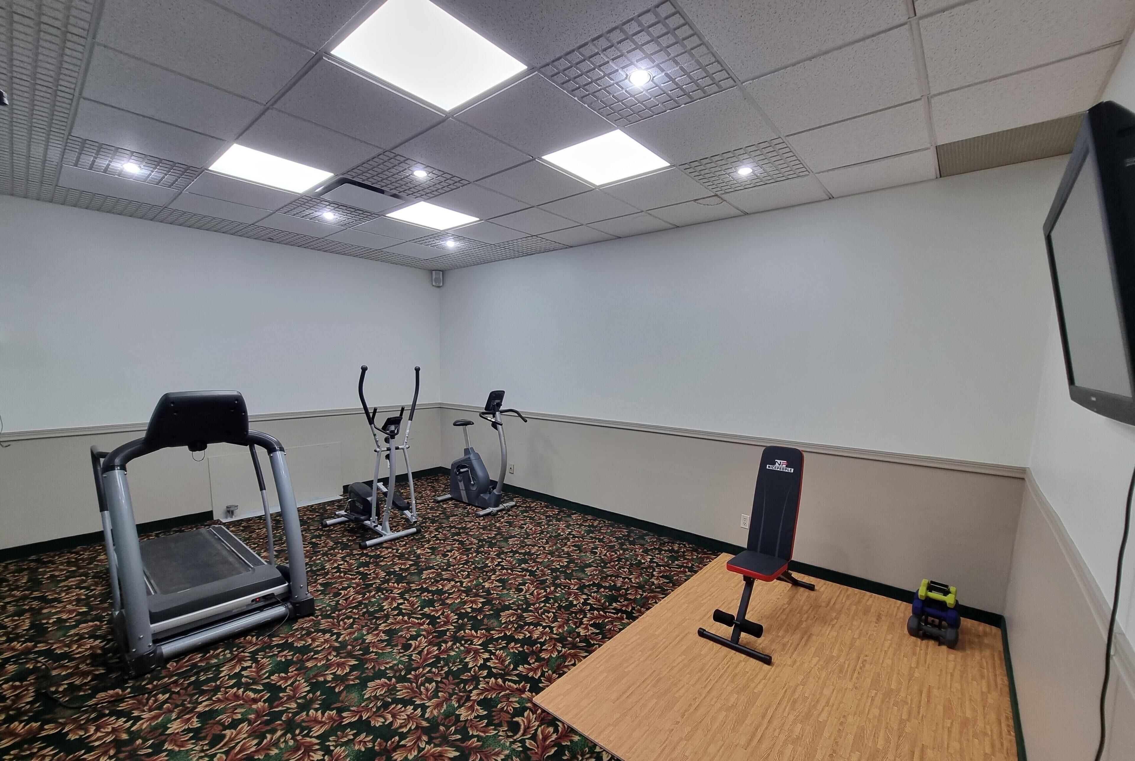 Un gimnasio con cinta de correr, elíptica y banco.