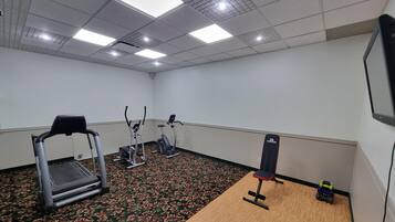 A fitness room with a treadmill, elliptical, and a bench.