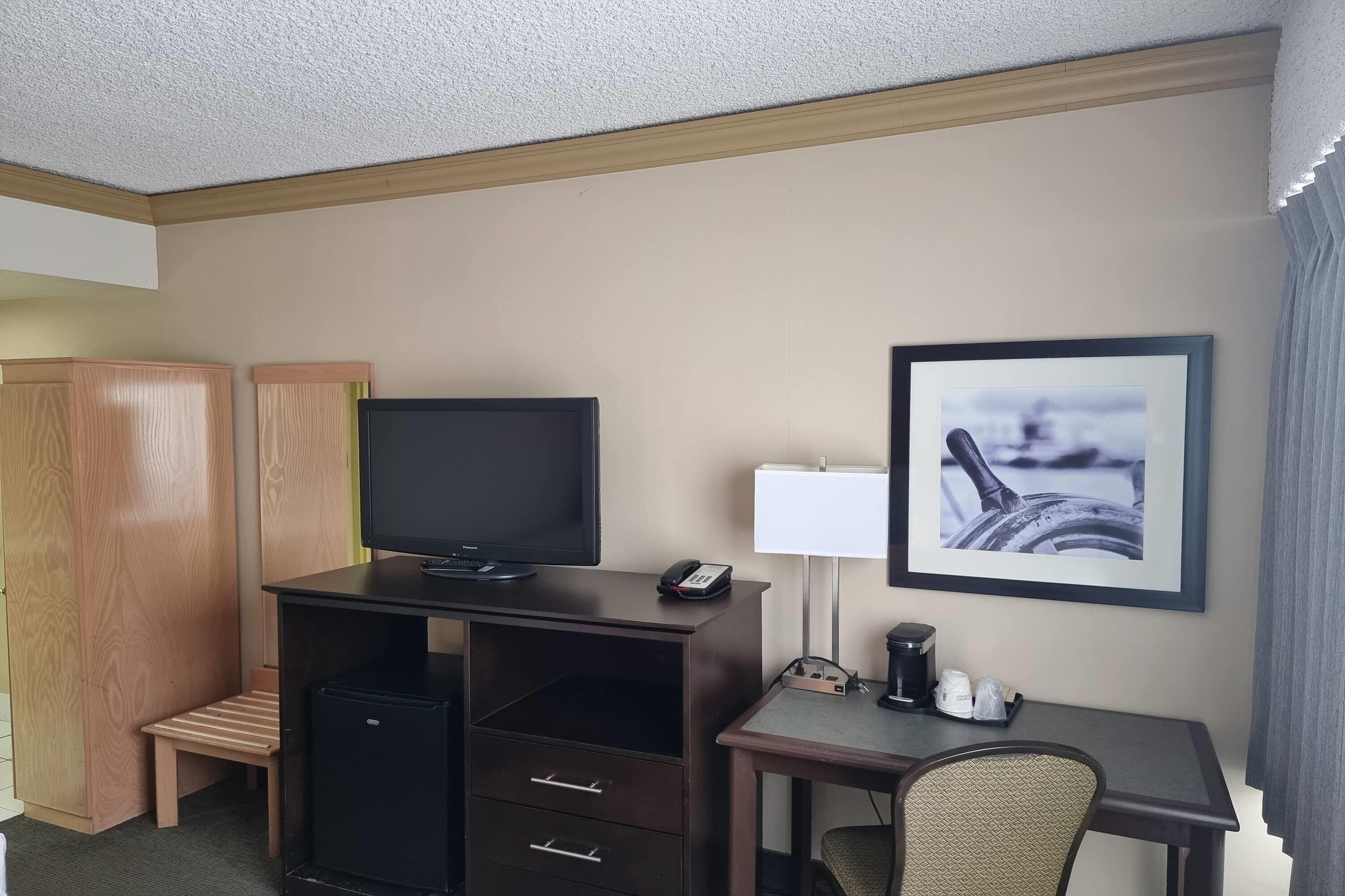 Habitació d'hotel amb escriptori, televisió, cadira, taula petita amb lamp i quadre al mur.