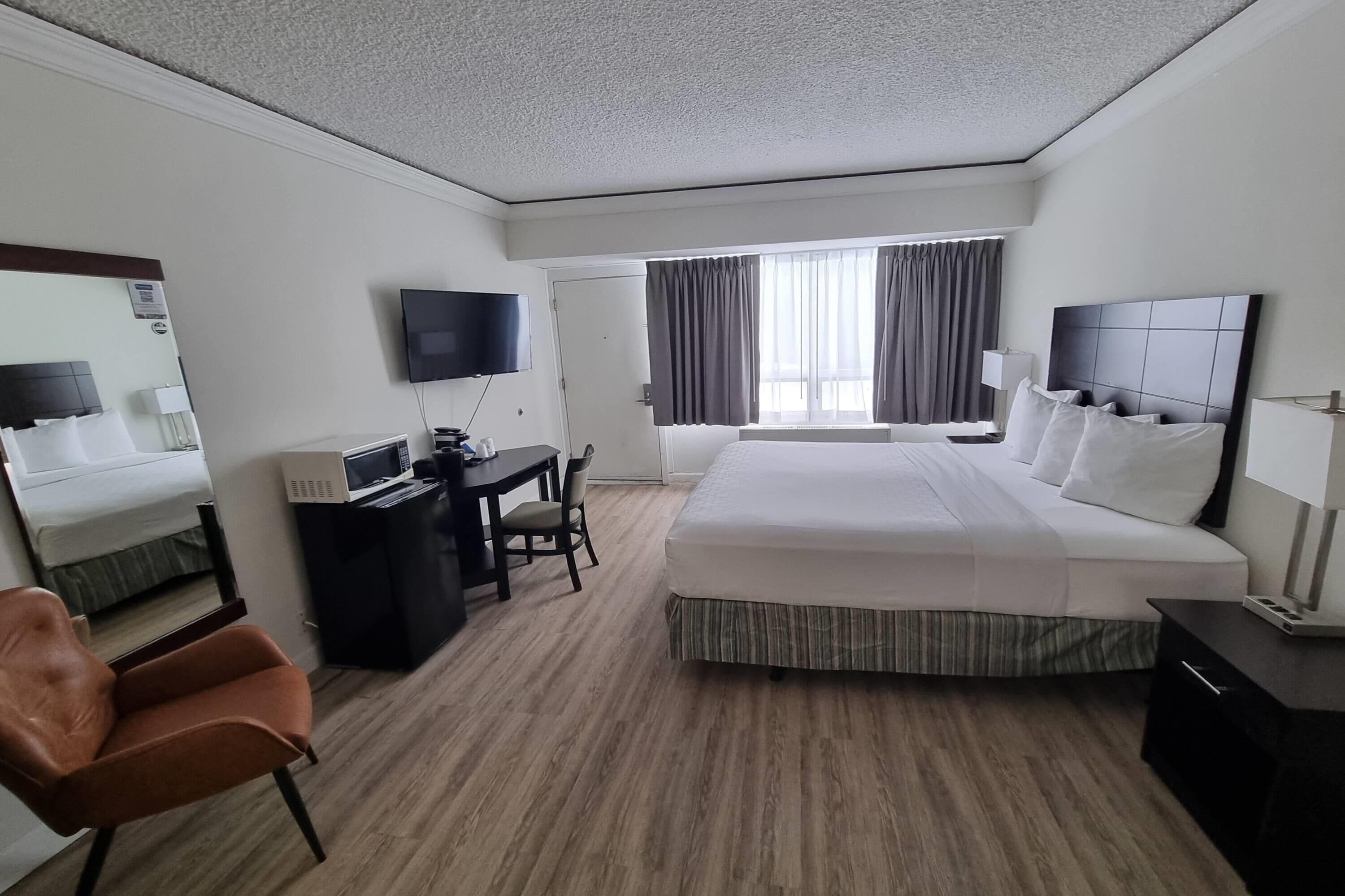 Une chambre d’hôtel avec un grand lit, un bureau avec une chaise, une télévision et une fenêtre avec des rideaux.