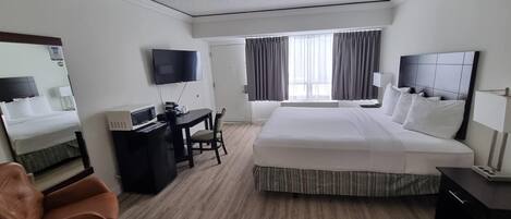 Une chambre d’hôtel avec un grand lit, un bureau avec une chaise, une télévision et une fenêtre avec des rideaux.