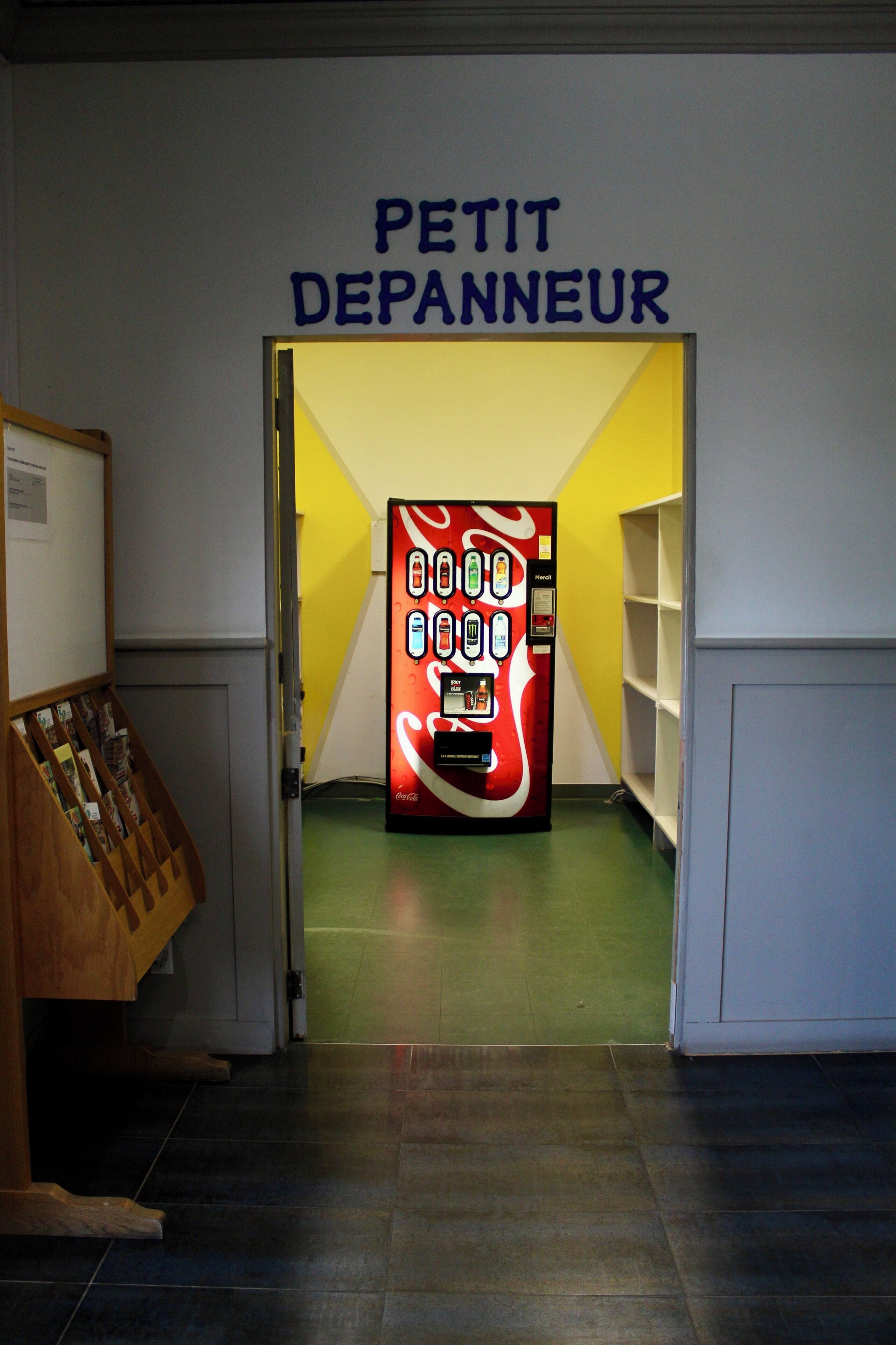 A hallway with a vending machine and a sign that reads 'PETIT DEPANNEUR'.