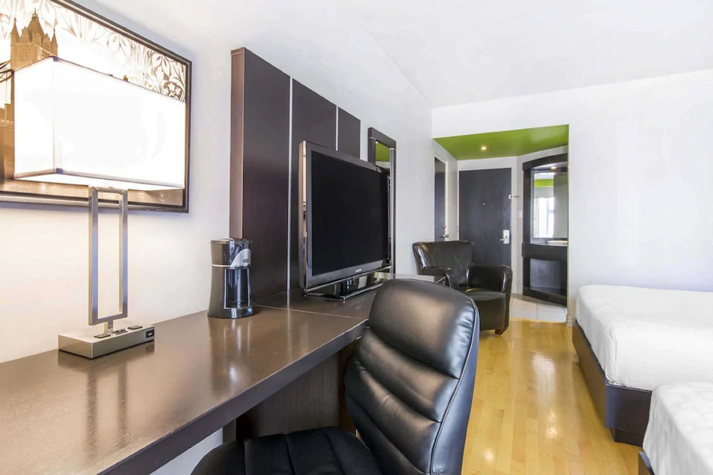Habitación de hotel con cama, escritorio, televisor de pantalla plana, silla y ventana grande con vista a un edificio.