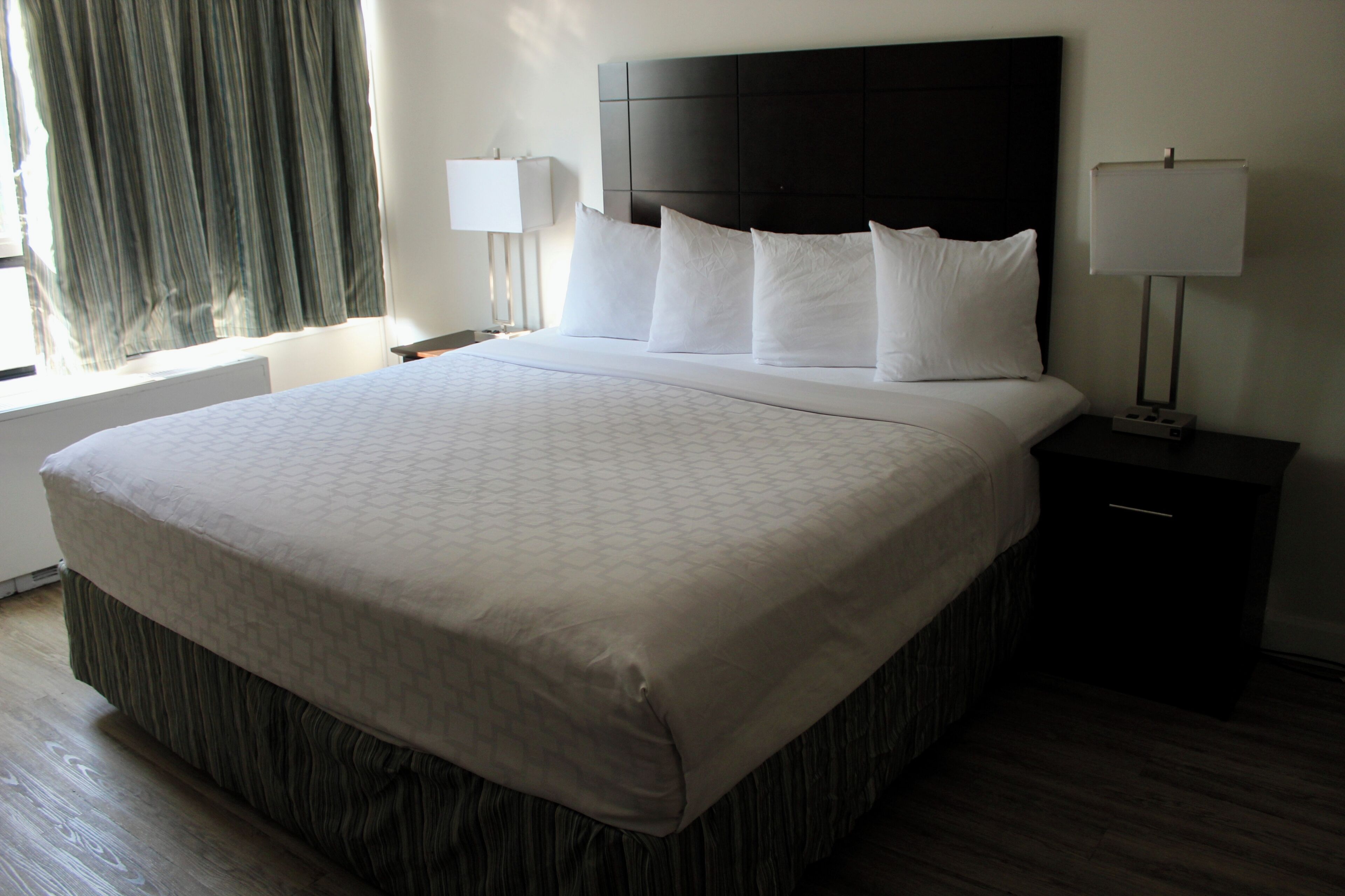 A hotel room with a large bed, two bedside lamps, a window with curtains, and a nightstand.