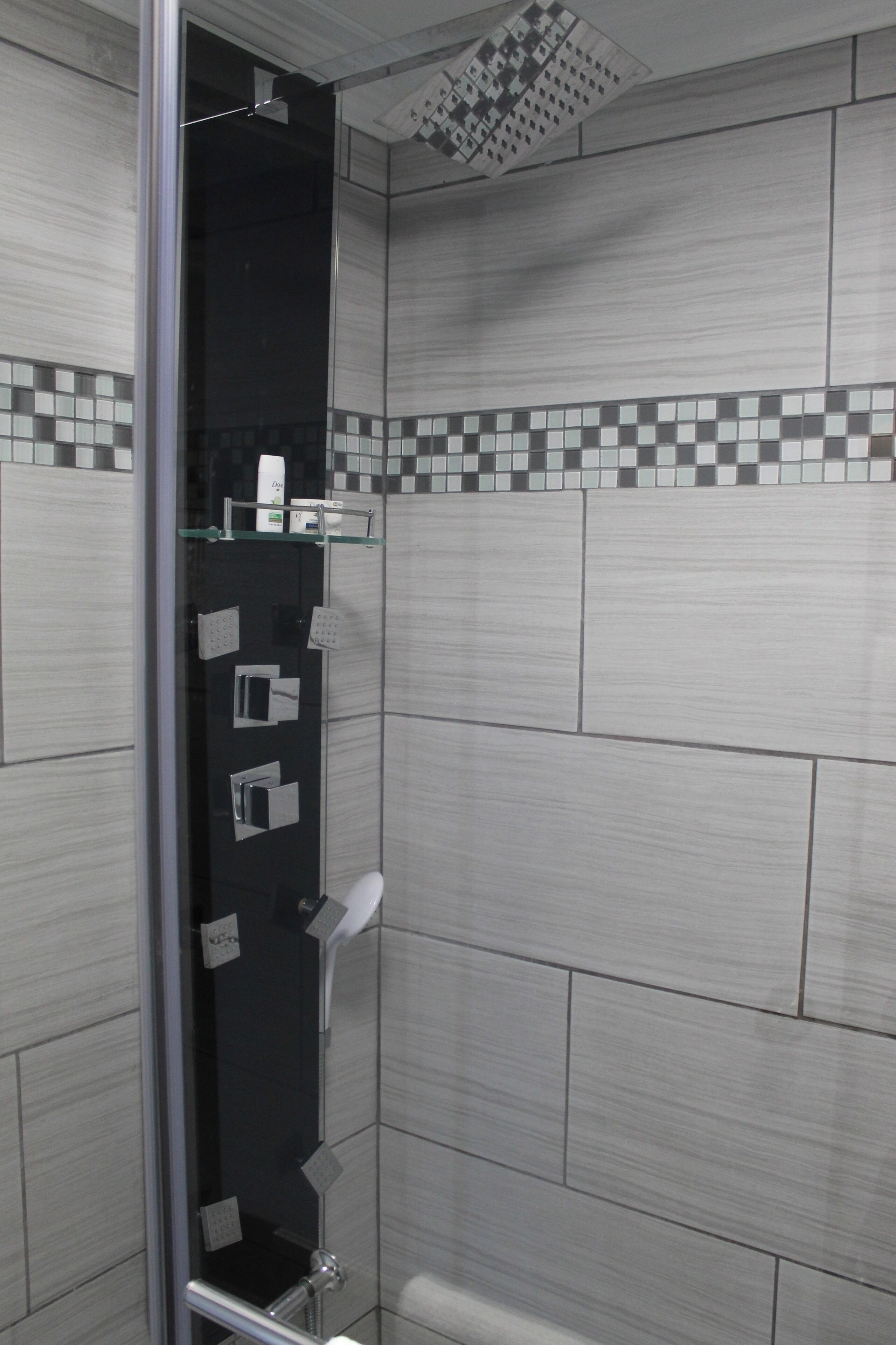A modern shower with a glass door, chrome fixtures, and a tiled wall with a checkered pattern.