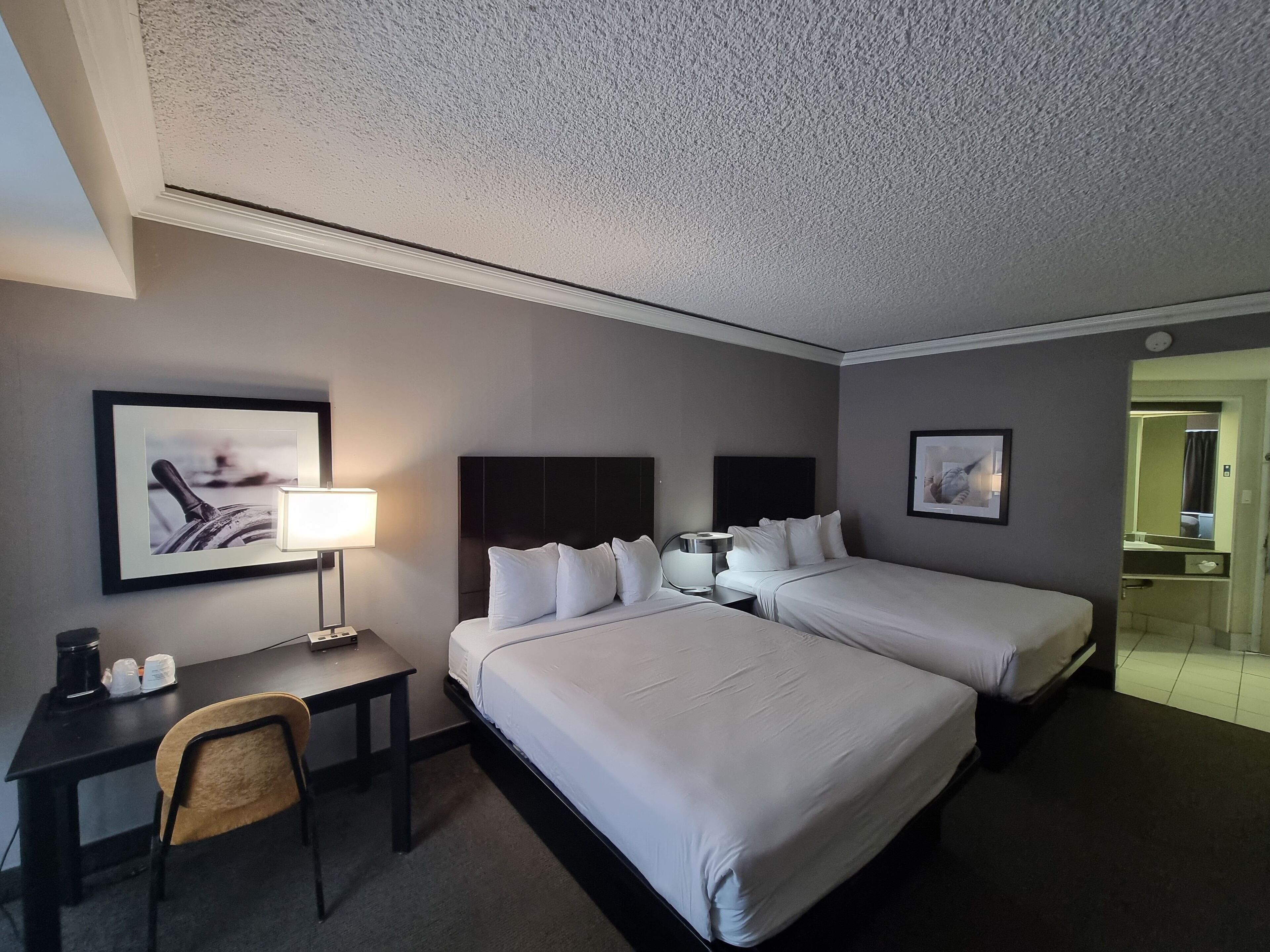 Una habitación de hotel con dos camas, un escritorio, una silla y una lámpara.