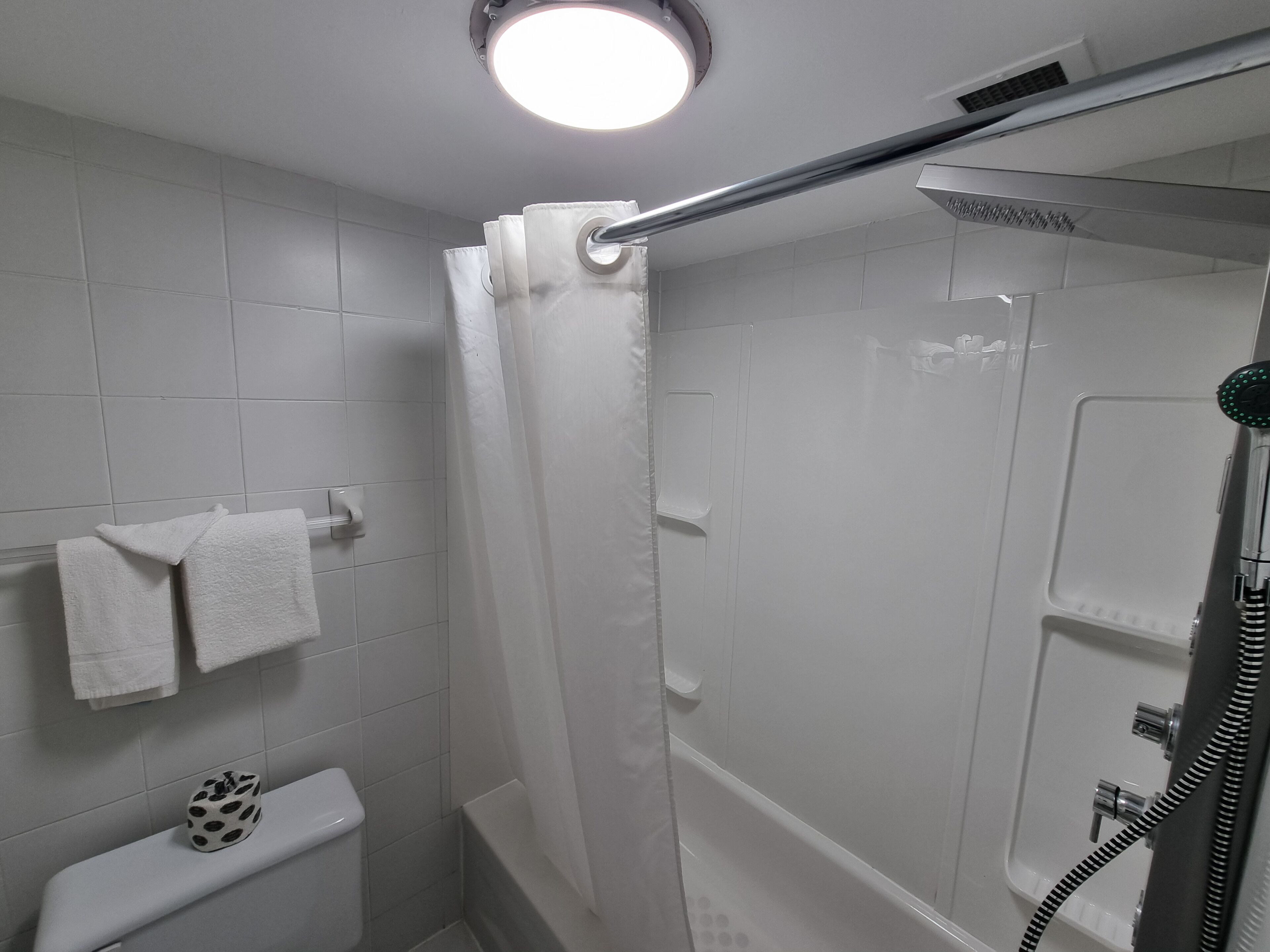 A modern bathroom with white tiles, a shower with a glass door, a toilet, and a towel rack with two towels.