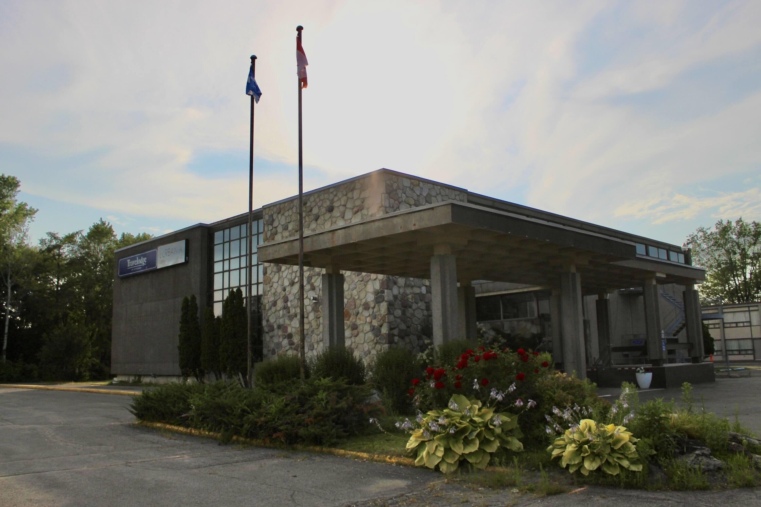 A building with a stone facade, a covered entrance, and a flagpole with flags.