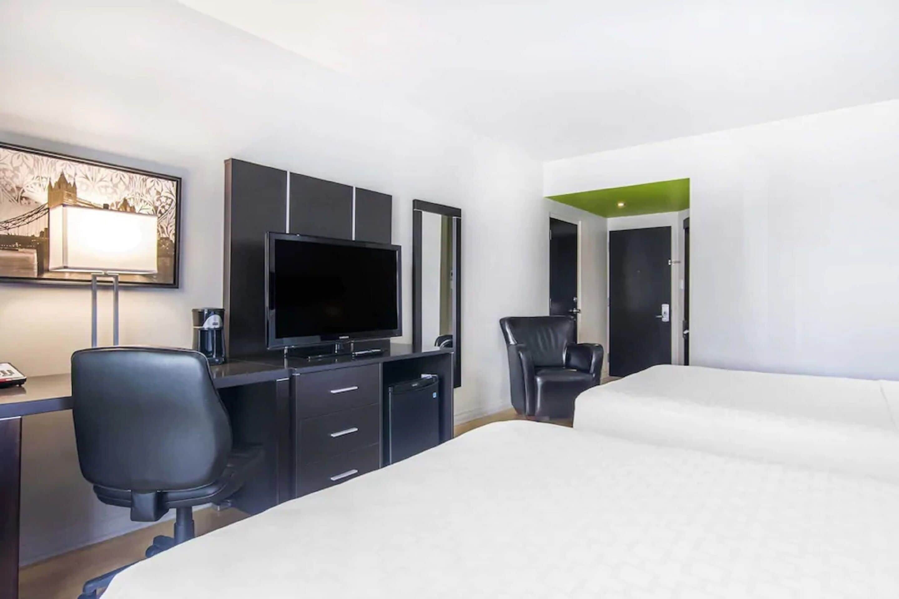 Une chambre d’hôtel avec un lit, un bureau avec un ordinateur, une télévision, une chaise et une porte.