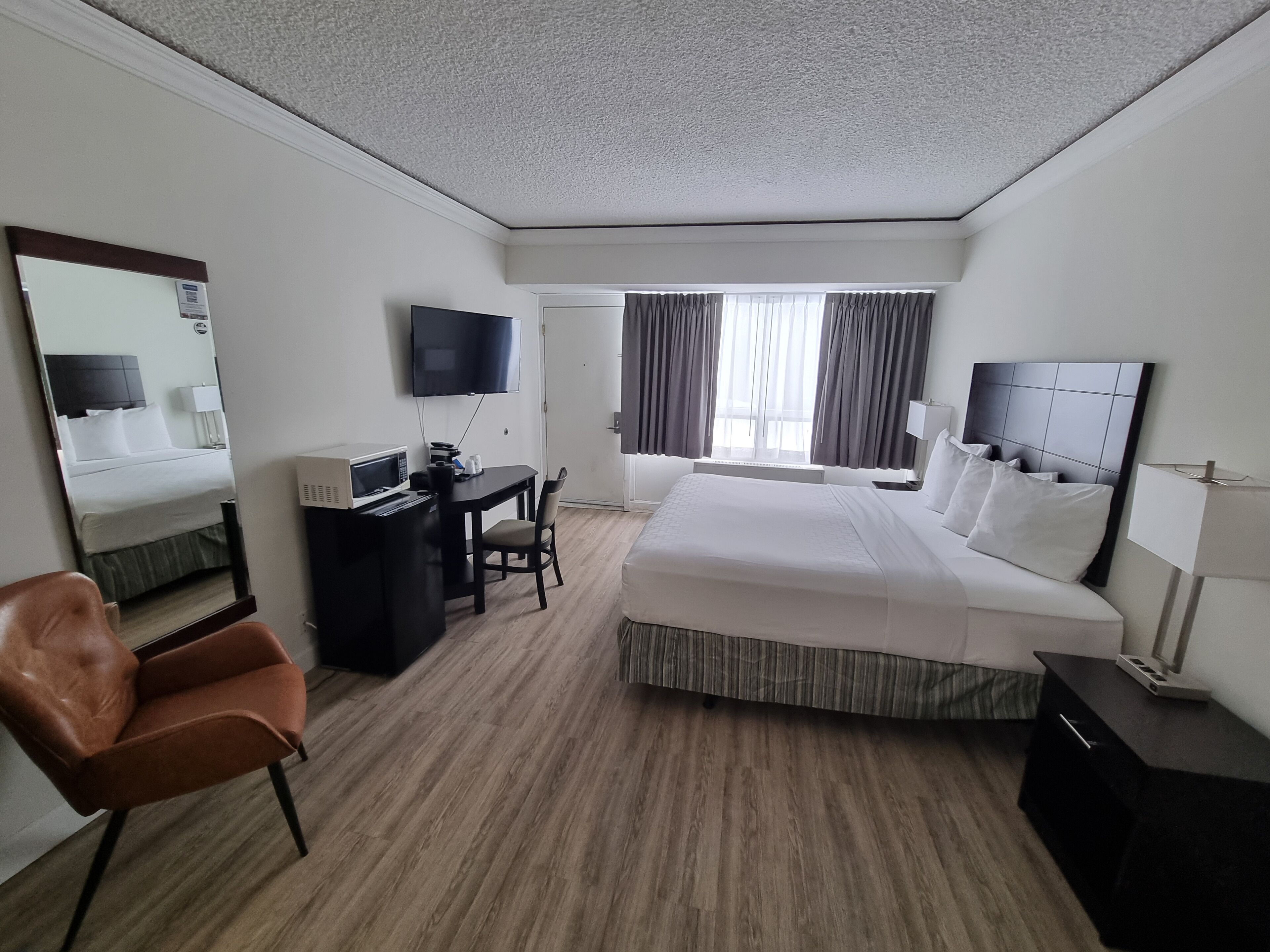 Habitación de hotel con una cama grande, un escritorio con computadora, televisor y ventana con cortinas.